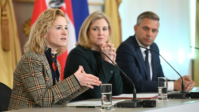 Wissenschaftsministerin Eva-Maria Holzleitner, Außenministerin Beate Meinl-Reisinger und Wirtschaftsminister Wolfgang Hattmannsdorfer mit Mikrofon bei der Pressekonferenz