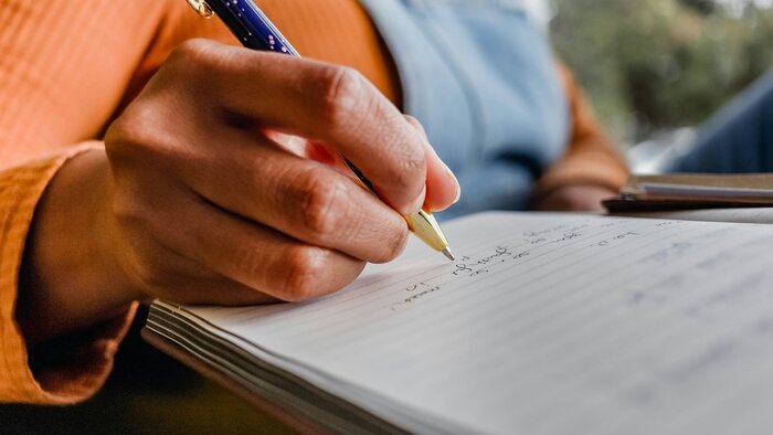 Großaufnahme einer Hand, die mit einem Kugelschreiber Notizen in ein Heft macht