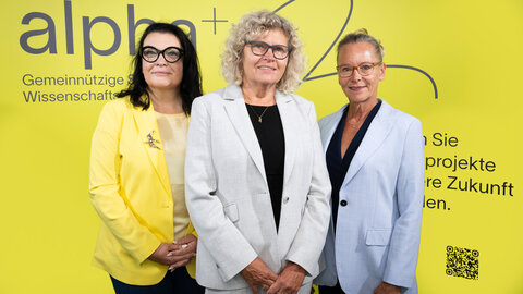 Das neue Vorstandsteam Ursula Jakubek, Sabine Seidler und Susanne Müller-Taborsky vor gelber Logowand der alpa+ Stiftung 
