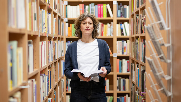 Alina Brad mit einem aufgeschlagenen Buch in einer Bibliothek.