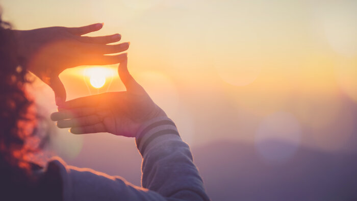 Eine Frau bildet mit ihren Händen einen Rahmen um die untergehende Sonne