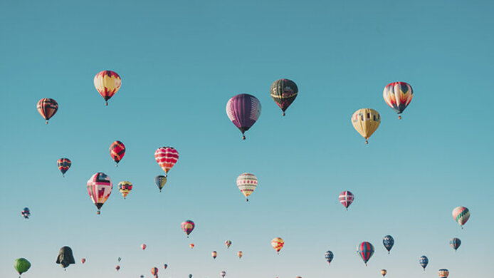 Viele bunte Heißluftballons aus der Froschperspektive am blauen Himmel