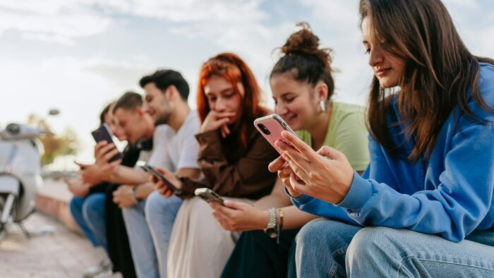 junge Menschen sitzen am Straßenrand und scrollen durch die Sozialen Medien auf ihren Handys