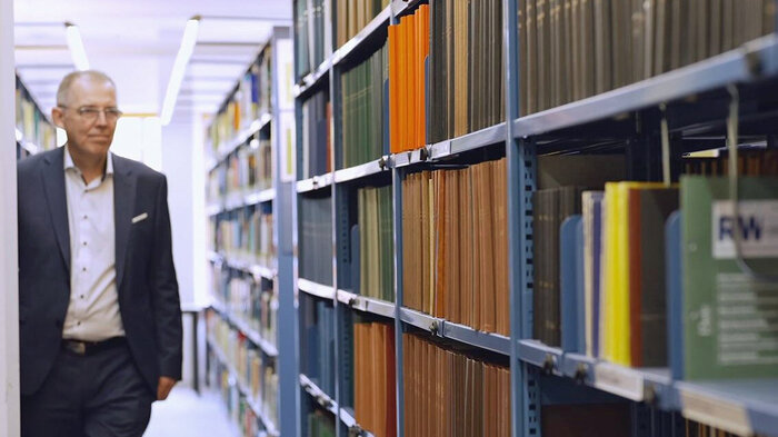 Michael Lang steht neben einem Regal einer Bibliothek