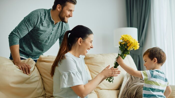 Glückliche Mutter, die zu Hause von ihrem kleinen Sohn einen Strauß gelber Blumen erhält. 