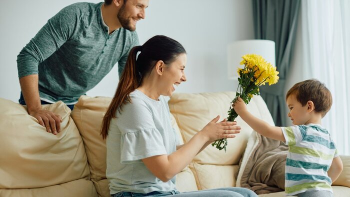 Glückliche Mutter, die zu Hause von ihrem kleinen Sohn einen Strauß gelber Blumen erhält. 