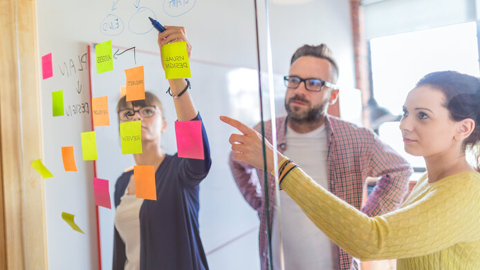 Drei Personen hinter einer Glaswand mit Post-Its