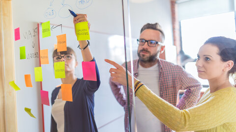 Drei Personen hinter einer Glaswand mit Post-Its