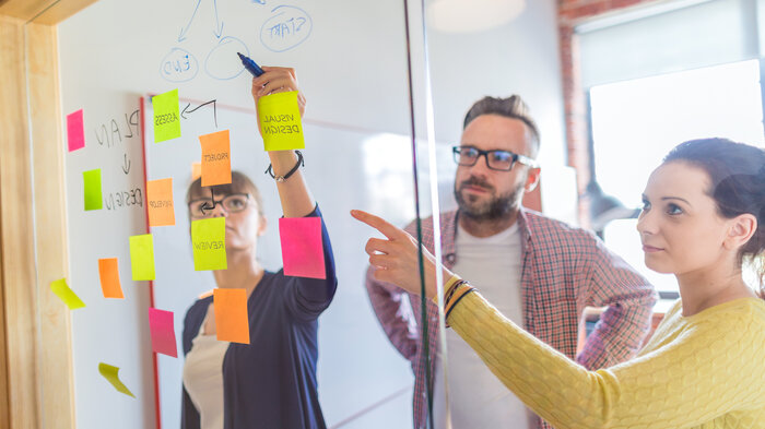 Drei Personen hinter einer Glaswand mit Post-Its