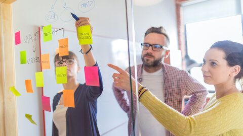 Drei Personen hinter einer Glaswand mit Post-Its