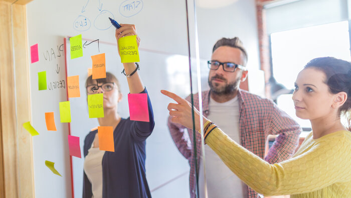 Drei Personen hinter einer Glaswand mit Post-Its