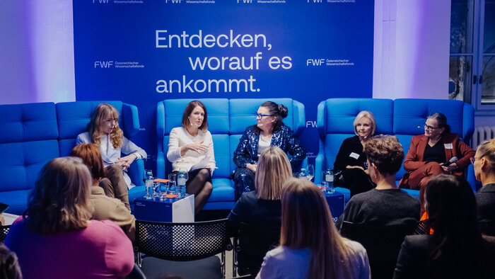 Fünf Frauen auf blauen Sofas diskutieren vor Publikum