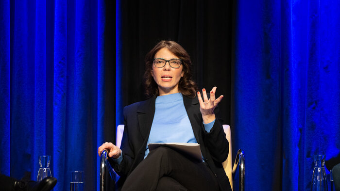 Francesca Ferlaino sitzend auf einer B&uuml;hne vor blauem Vorhang