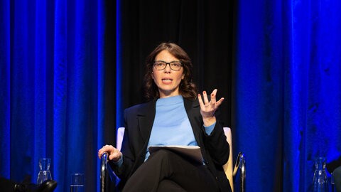 Francesca Ferlaino sitzend auf einer Bühne vor blauem Vorhang