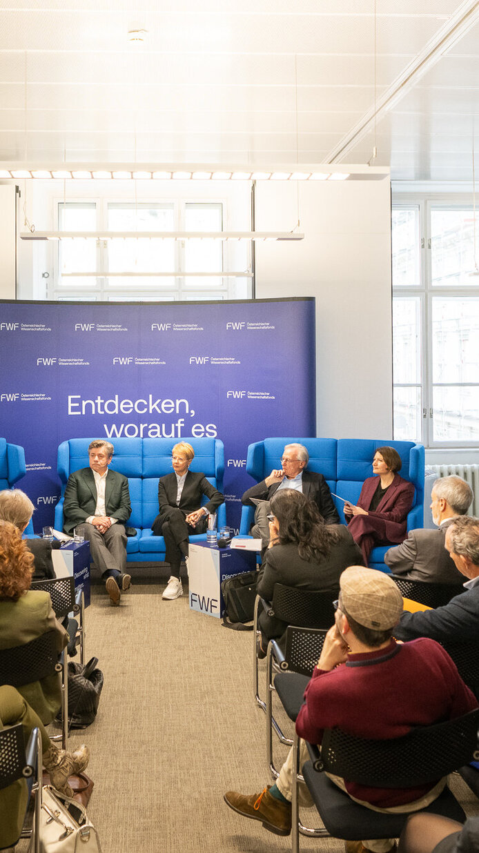 Die Teilnehmer:innen von hinten. Im Hintergrund die Speaker:innen während der Diskussion.