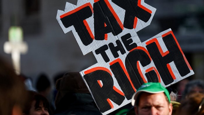 Ein Demonstrant h&auml;lt bei einer Protestkundgebung gegen Rentenk&uuml;rzungen und Arbeitsmarktreformen ein Plakat mit der Aufschrift &bdquo;Besteuert die Reichen&ldquo; hoch