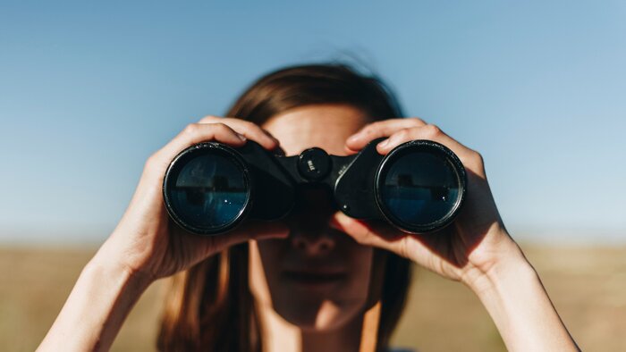 Frau hält mit beiden Händen ein Fernglas vor die Augen und schaut durch