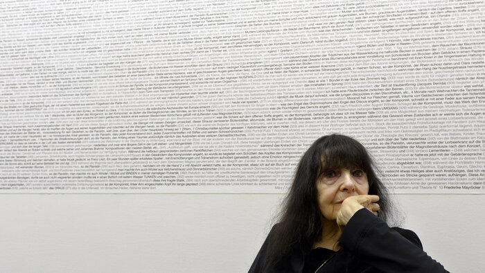 Schwarz-weiß-Aufnahme der Schriftstellerin Friederike Mayröcker im Alter von 90 Jahren vor einer Wand mit Wörtern