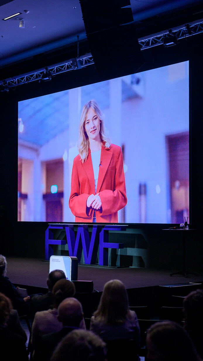 Ansicht von hinten rechts aufs Publikum und auf die Leinwand mit dem Exzellenzcluster-Video