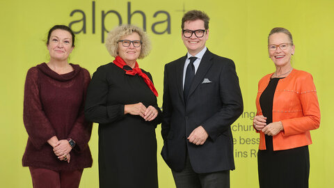 Ursula Jakubek, Sabine Seidler, Christoph Neumayer und Susanne Müller-Taborsky vor der gelben Logowand der alpha+-Stiftung