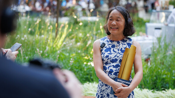 Elly Tanaka mit ihrem Science Award im Arm vor einer Grünfläche im Arkadenhof des Rathauses