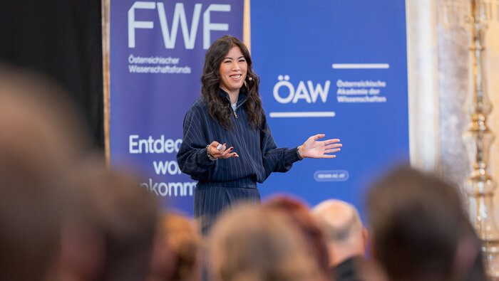 Mai Thi Nguyen-Kim auf der B&uuml;hne vor den blauen Logow&auml;nden von FWF und &Ouml;AW
