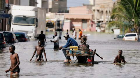 Überflutete Straße in Dakar, Westafrika - Menschen waten durch Wasser, das bis zum Nabel reicht