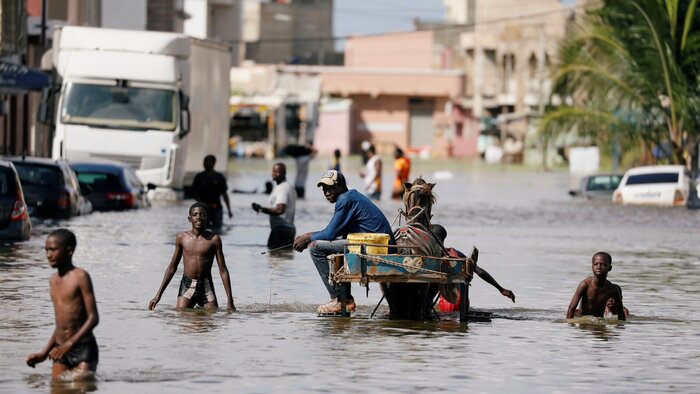 &Uuml;berflutete Stra&szlig;e in Dakar, Westafrika - Menschen waten durch Wasser, das bis zum Nabel reicht