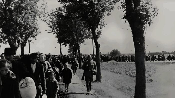 1939, schwarz-weiß-Bild: langer Menschenzug marschiert durch eine Allee Richtung Bahnhof: Familien, Kinder, Erwachsene werden in Polen zwangsumgesiedelt.