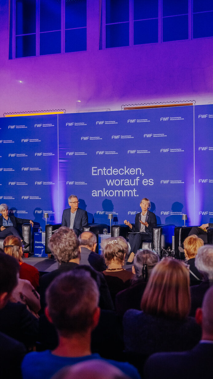 Hannelore Veit, Manuela Baccarini, Christian Pohl, Barbara Weitgruber, Mari Sundli Tveit und FWF-Präsident Christof Gattringer auf der Bühne im Hintergrund. Teilnehmer:innen im Vordergrund.