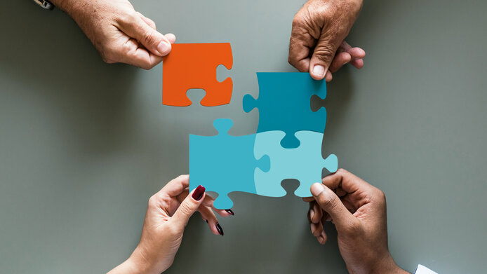 Vier Hände fügen vier bunte Puzzleteile zusammen