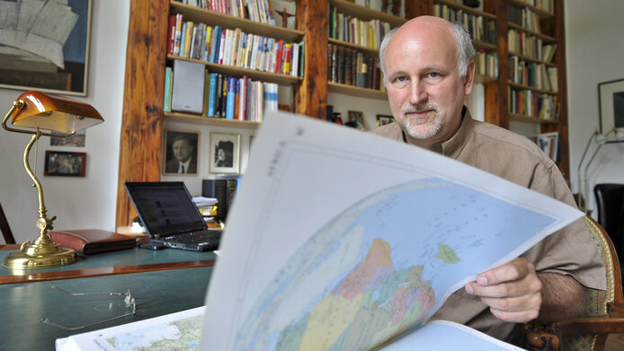 Wolfgang Lutz blättert in einem großen Atlas