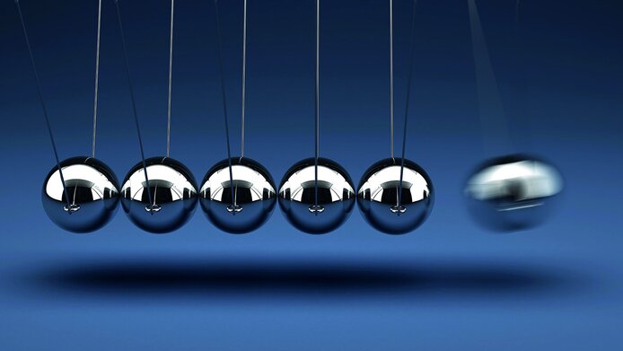 Nahaufnahme eines Kugelstoßpendels (Newton) mit sechs silberfarbenen Metallkugeln vor blauem Hintergrund