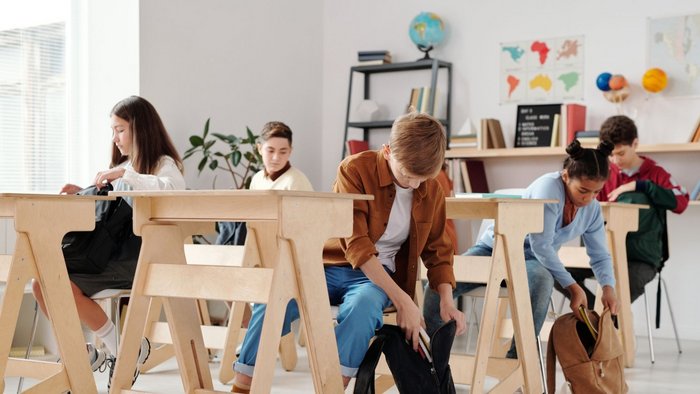 Junge Sch&uuml;ler:innen im Klassenzimmer packen ihre Rucks&auml;cke ein