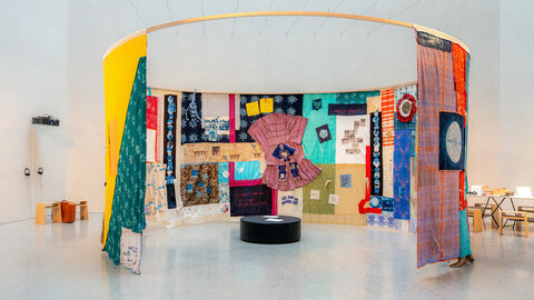 Ein großer Quilt mit bunten Stoffen und vielen Mustern hängt in einem Museum von der Decke