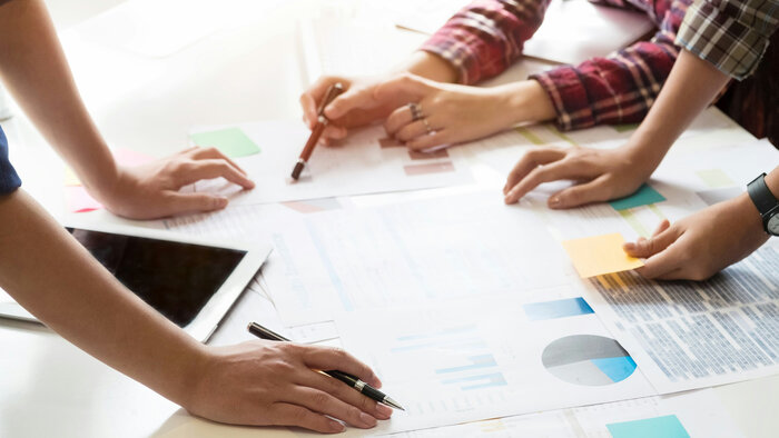 Drei Paar H&auml;nde mit Tablet, Stiften und Unterlagen auf einem Schreibtisch