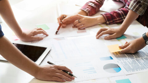 Drei Paar Hände mit Tablet, Stiften und Unterlagen auf einem Schreibtisch