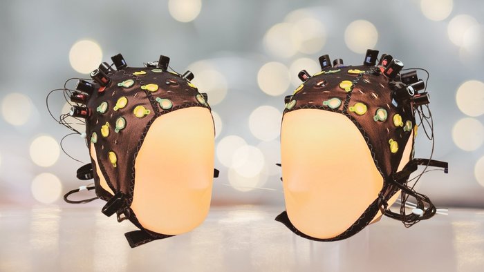 Zwei beleuchtete Kopfpuppen sind aufeinander gerichtet und haben EEG-M&uuml;tzen auf, um ihre Gehirnaktivit&auml;t zu messen. 
