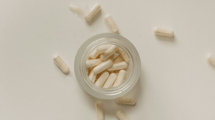 Tabletten in Kapselform, die am Tisch verstreut und in einem Glasbehälter liegen