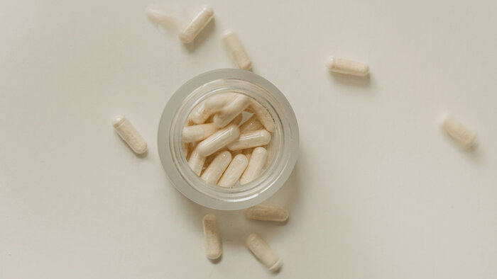 Tabletten in Kapselform, die am Tisch verstreut und in einem Glasbehälter liegen