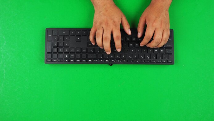 Hände tippen auf schwarzer Tastatur vor grünem Hintergrund