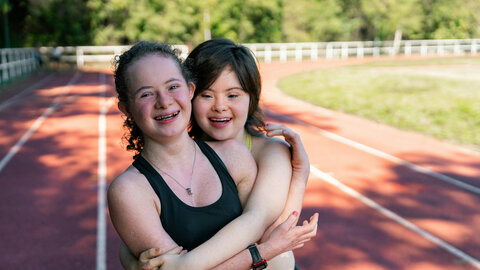 Zwei Mädchen, eines mit Down-Syndrom, umarmen und freuen sich am Sportplatz