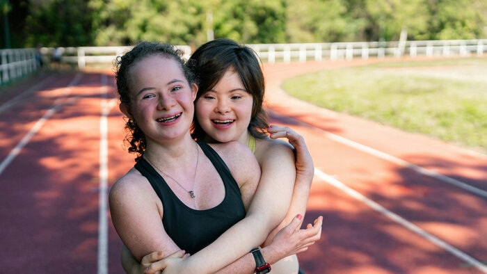 Zwei M&auml;dchen, eines mit Down-Syndrom, umarmen und freuen sich am Sportplatz