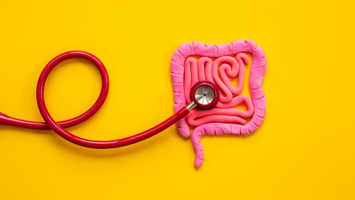 Ein rotes Stethoskop auf einem pinken Plastilindarm auf sonnengelbem Hintergrund