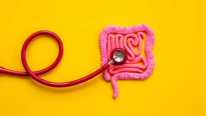 Ein rotes Stethoskop auf einem pinken Plastilindarm auf sonnengelbem Hintergrund