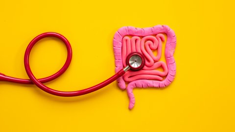 Ein rotes Stethoskop auf einem pinken Plastilindarm auf sonnengelbem Hintergrund